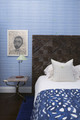 Side view of a bedroom featuring Fogo Island Collection's We Sailed Away wallpaper in blue, with a wooden headboard.